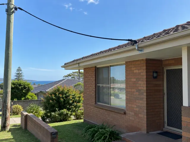 Overhead service cable and point-of-attachment bracket on a brick house exterior in Collaroy