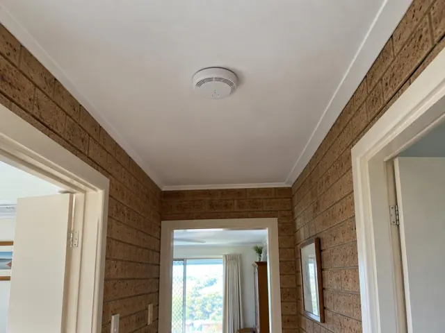 Ceiling smoke alarm in a hallway with brick walls and white door frames in Dee Why